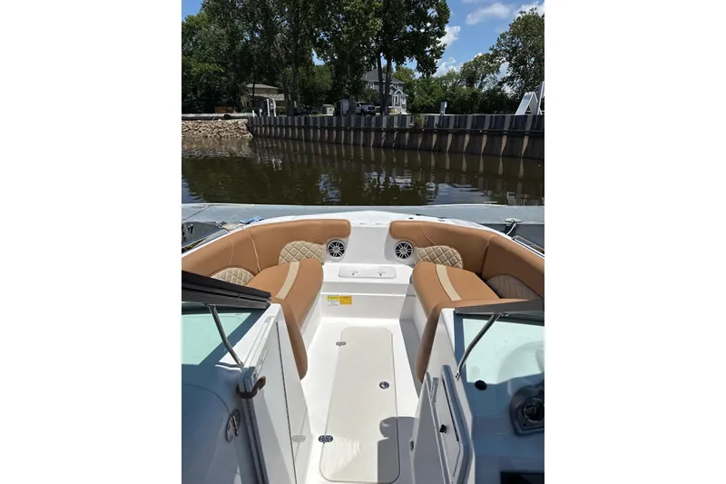 Slide: The Image of 2025 NauticStar 223 DC Deck boat interior with tan seating, docked by a calm river. - 3