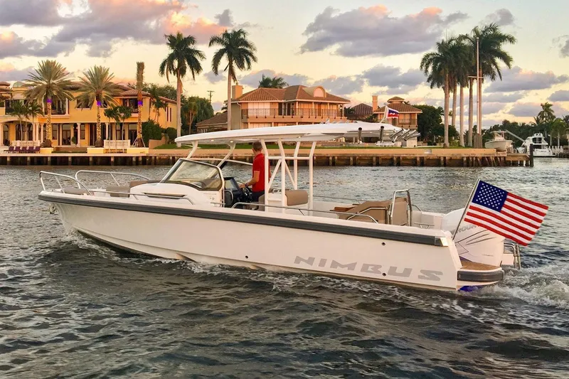 The Image of 2025 Nimbus T9 boat cruising near waterfront homes, displaying an American flag. - 0