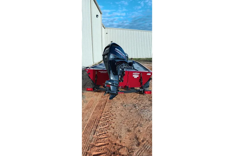 Slide: The Image of 2026 Tracker Panfish 17 boat with Mercury engine, parked on dirt near a building. - 12