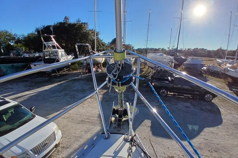 Slide: The Image of 1983 Wauquiez Hood sailboat in a sunny boatyard, surrounded by vehicles and other boats. - 49
