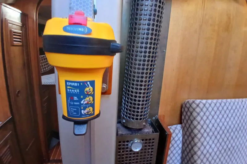 Slide: The Image of Yellow EPIRB device inside 1983 Wauquiez Hood boat cabin, near metal vent and wooden paneling. - 5