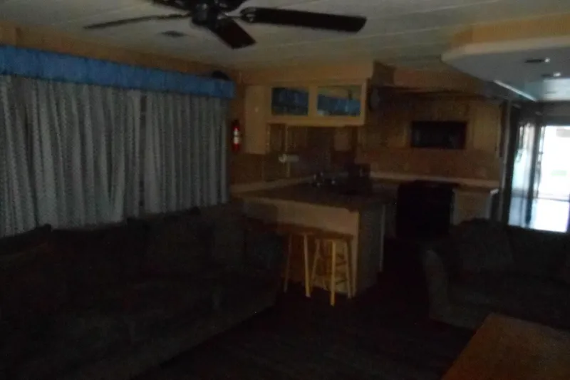 Slide: The Image of Dimly lit interior of a 1991 Stardust Cruisers 7516 houseboat with kitchen and seating area. - 3