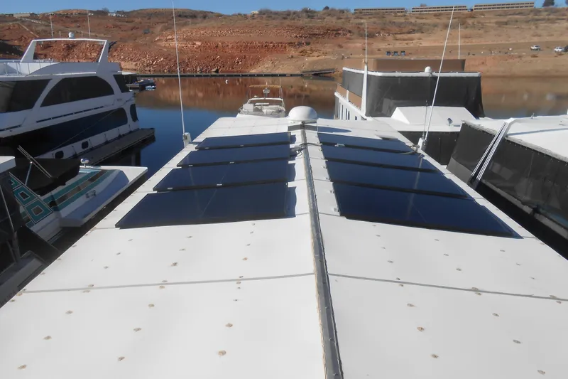 Slide: The Image of Houseboat with solar panels on roof, docked in a scenic lake setting. Stardust Cruisers 7516, 1991. - 35
