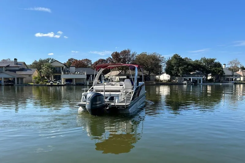 Slide: The Image of 2021 Bennington 25 RXSBA pontoon boat on a calm lake near waterfront homes. - 15