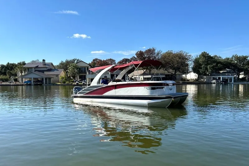 Slide: The Image of 2021 Bennington 25 RXSBA pontoon boat on a calm lake with houses in the background. - 18