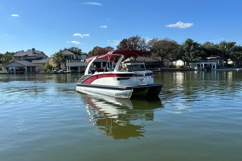 Slide: The Image of 2021 Bennington 25 RXSBA pontoon boat on a calm lake with houses in the background. - 19