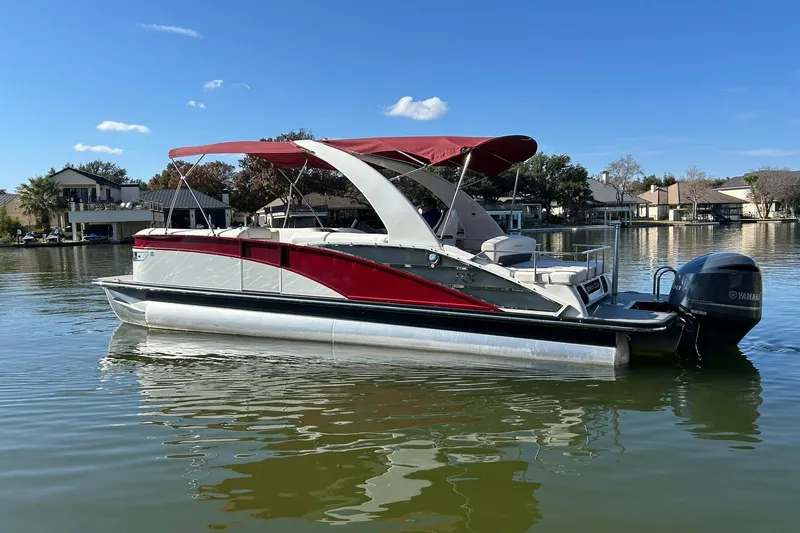 Slide: The Image of 2021 Bennington 25 RXSBA pontoon boat with red canopy on a calm lake. - 2