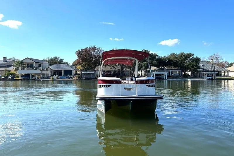 Slide: The Image of 2021 Bennington 25 RXSBA pontoon boat on a calm lake with houses in the background. - 21