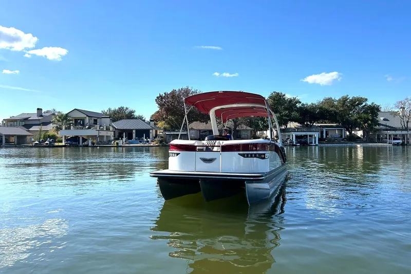 Slide: The Image of 2021 Bennington 25 RXSBA pontoon boat on a serene lake with waterfront homes. - 22