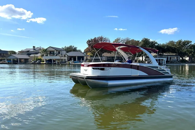 Slide: The Image of 2021 Bennington 25 RXSBA pontoon boat on a serene lake with waterfront homes. - 24