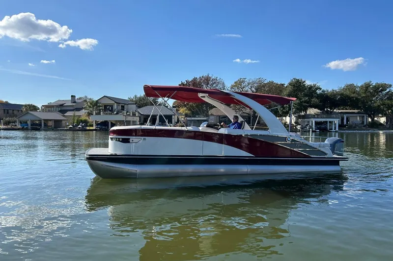 Slide: The Image of 2021 Bennington 25 RXSBA pontoon boat on a calm lake under a clear blue sky. - 25
