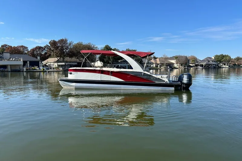 Slide: The Image of 2021 Bennington 25 RXSBA pontoon boat on a calm lake with a red canopy. - 6