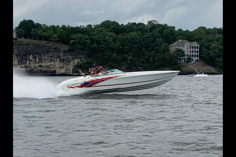 The Image of 2000 Formula 353 FASTech speedboat cruising on a lake with passengers, near a wooded shoreline. - 0