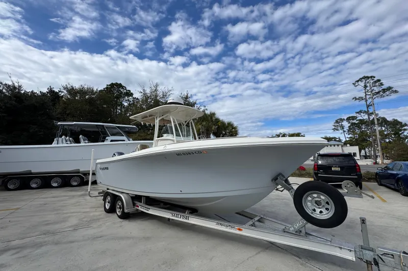 Slide: The Image of 2020 Sailfish 242 CC boat on trailer, parked outdoors under a partly cloudy sky. - 8