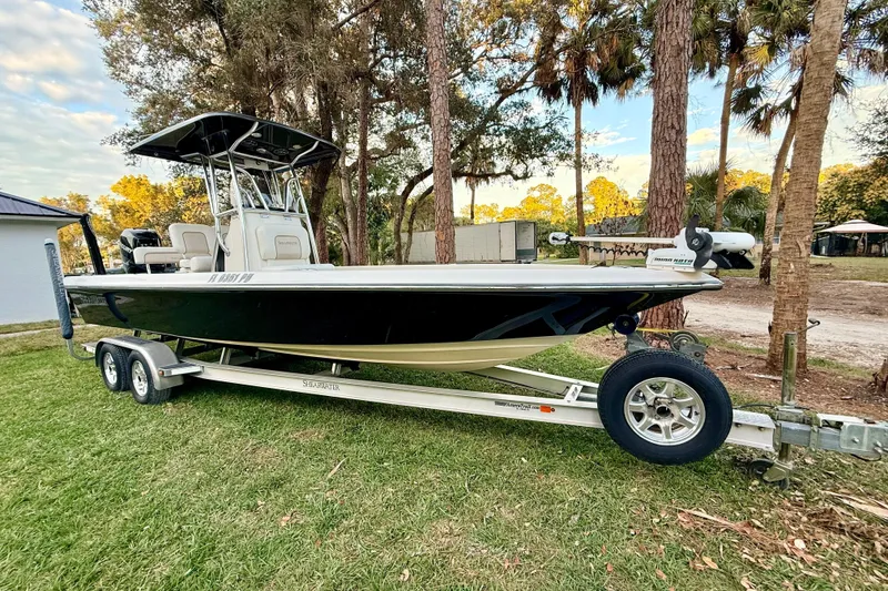 The Image of 2012 ShearWater 25LTZ boat on trailer, parked on grass with trees in background. - 2