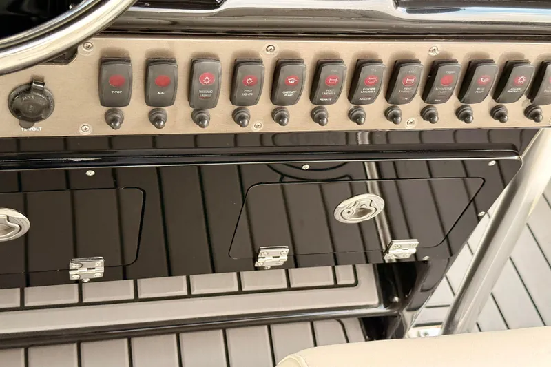 Slide: The Image of Control panel of a 2012 ShearWater 25LTZ boat with multiple switches and storage compartments. - 53