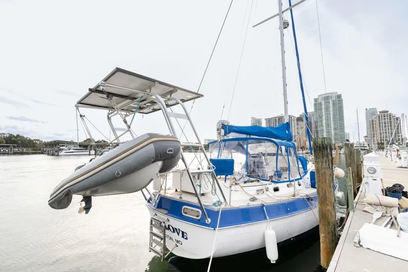 Slide: The Image of 1987 Morgan 41 Out Island Classic sailboat docked with dinghy, city skyline in background. - 2