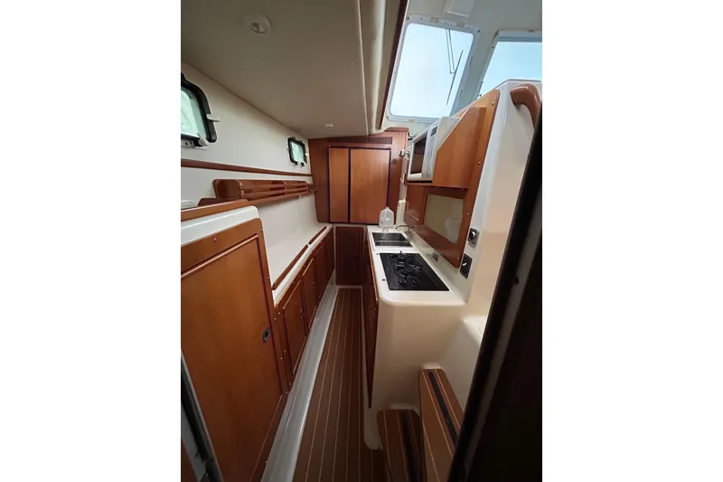 Slide: The Image of Interior of 2004 PDQ 34 Power Catamaran, featuring a compact kitchen with wood cabinetry. - 16