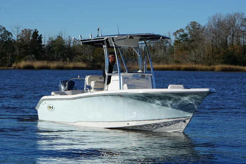 Slide: The Image of 2024 Sea Hunt Ultra 219 boat on calm water with trees in the background. - 11