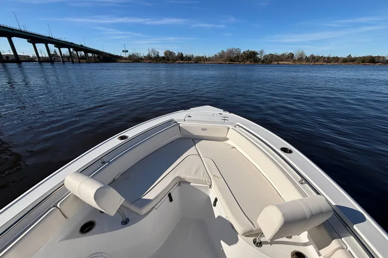 Slide: The Image of 2024 Sea Hunt Ultra 219 boat on calm water near a bridge under a clear blue sky. - 5