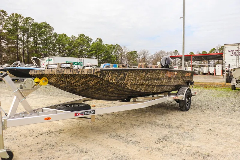 The Image of 2026 Excel Tomahawk boat on trailer, camo design, parked outdoors. - 0