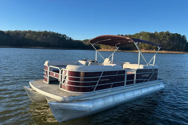 Slide: The Image of 2023 Godfrey Sweetwater 2286 C pontoon boat on a serene lake with forested shoreline. - 2