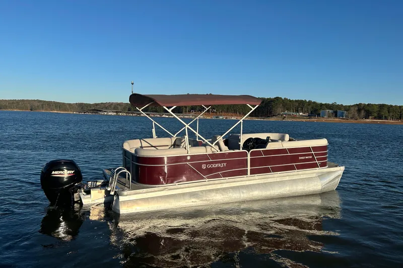 Slide: The Image of 2023 Godfrey Sweetwater 2286 C pontoon boat on a calm lake under clear blue sky. - 7