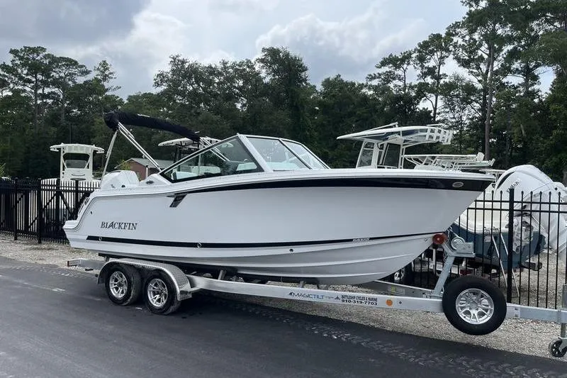 Slide: The Image of 2024 Blackfin 232 DC boat on trailer, parked outdoors near trees. - 1