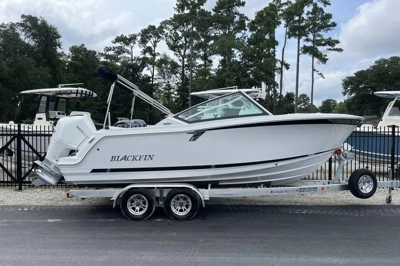 Slide: The Image of 2024 Blackfin 232 DC boat on trailer, parked outdoors near trees. - 2