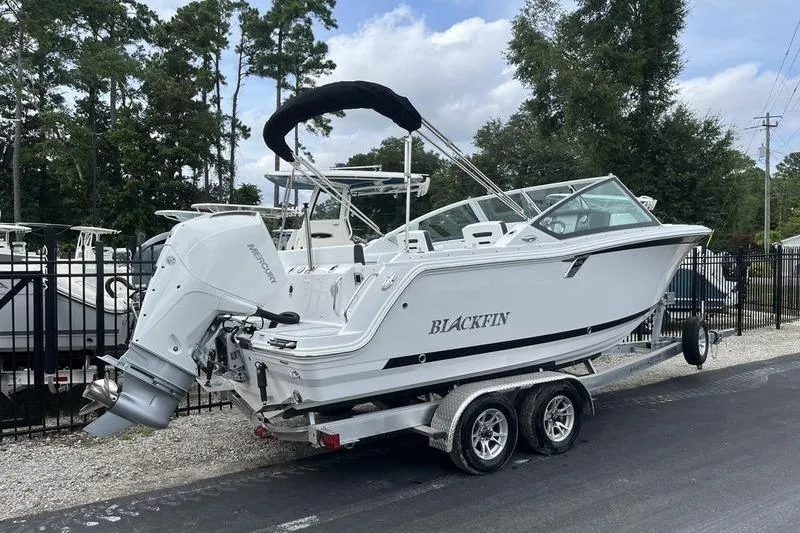 Slide: The Image of 2024 Blackfin 232 DC boat on trailer, parked outdoors near trees and fence. - 3