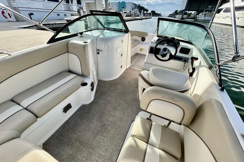 Slide: The Image of 2022 NauticStar 223 DC boat interior with beige seating and steering wheel, docked by water. - 8