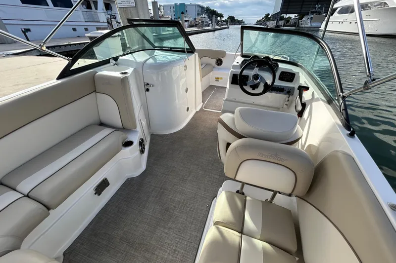 Slide: The Image of 2022 NauticStar 223 DC boat interior with beige seating and steering wheel, docked at marina. - 9
