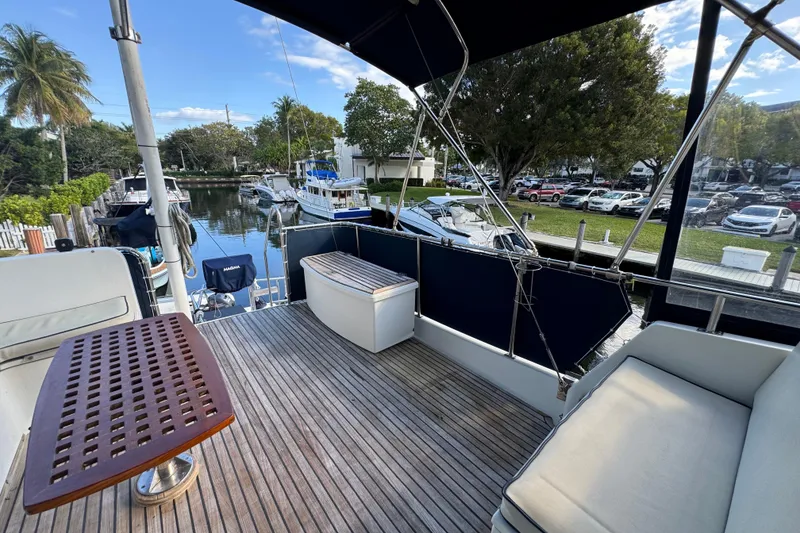 Slide: The Image of Deck of 1990 Grand Banks 46 Classic yacht with seating and table, docked near lush greenery. - 52