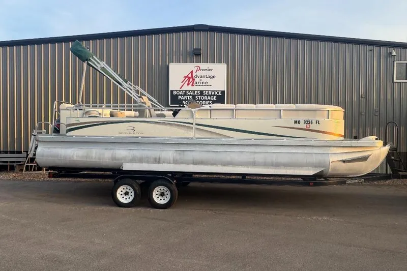The Image of 2002 Bennington 2550RL pontoon boat on trailer, parked outside a marine service building. - 0