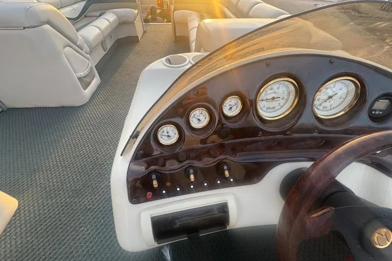 Slide: The Image of 2002 Bennington 2550RL boat dashboard with gauges and plush seating in sunlight. - 10