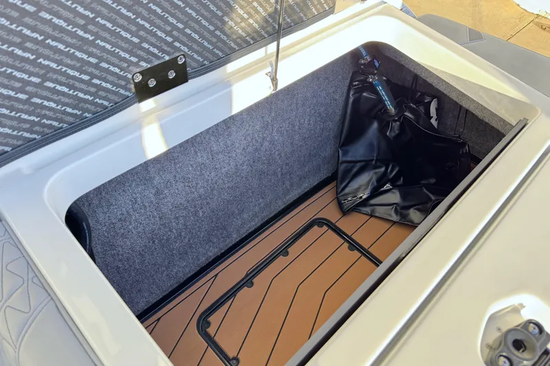 Slide: The Image of 2026 Nautique Super Air Nautique GS22 storage compartment with black bag and wooden flooring. - 25