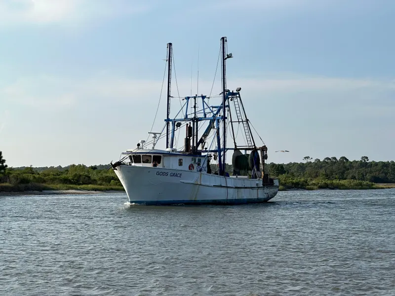 The Image of Commercial Butterfish Fishing Trawler, 1971, navigating calm waters near a lush shoreline. - 0