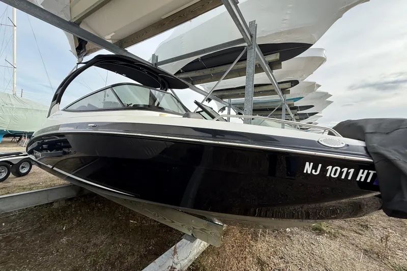 The Image of 2019 Yamaha Boats 242 Limited S in storage, black hull, covered, on a rack. - 1