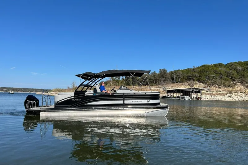 Slide: The Image of 2020 Harris FloteBote Solstice 230 pontoon boat on a calm lake under clear blue skies. - 2