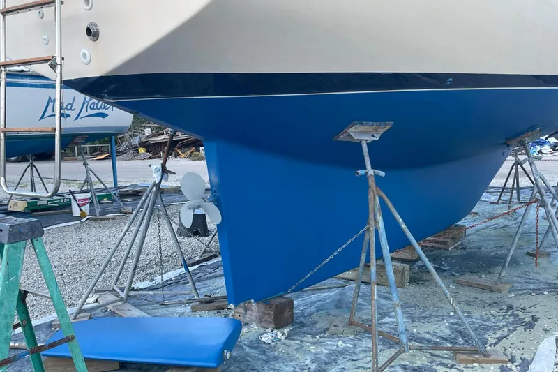 Slide: The Image of 1990 Island Packet 35 Cutter sailboat on stands, blue hull, in a boatyard. - 2