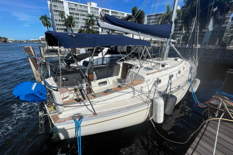 Slide: The Image of 1990 Island Packet 35 Cutter sailboat docked, featuring blue canopy and coastal backdrop. - 86