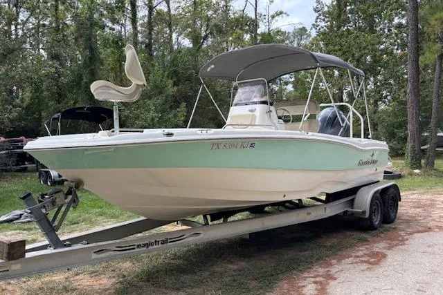 Slide: The Image of 2021 NauticStar 211 Hybrid boat on trailer, parked in wooded area. - 2