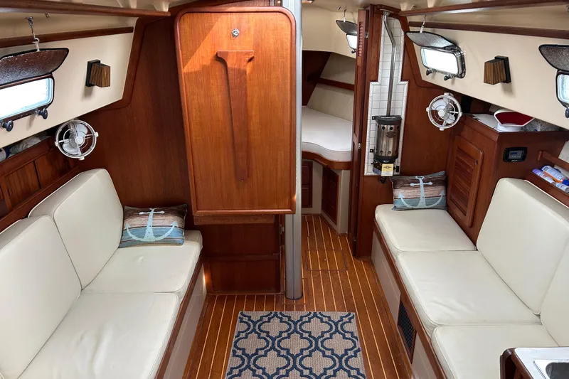 Slide: The Image of 1997 Island Packet 29 sailboat interior with wood finish and white seating. - 3