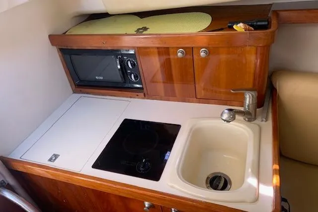 Slide: The Image of 2004 Mainship Pilot 30-II galley with sink, stove, microwave, and wooden cabinetry. - 13