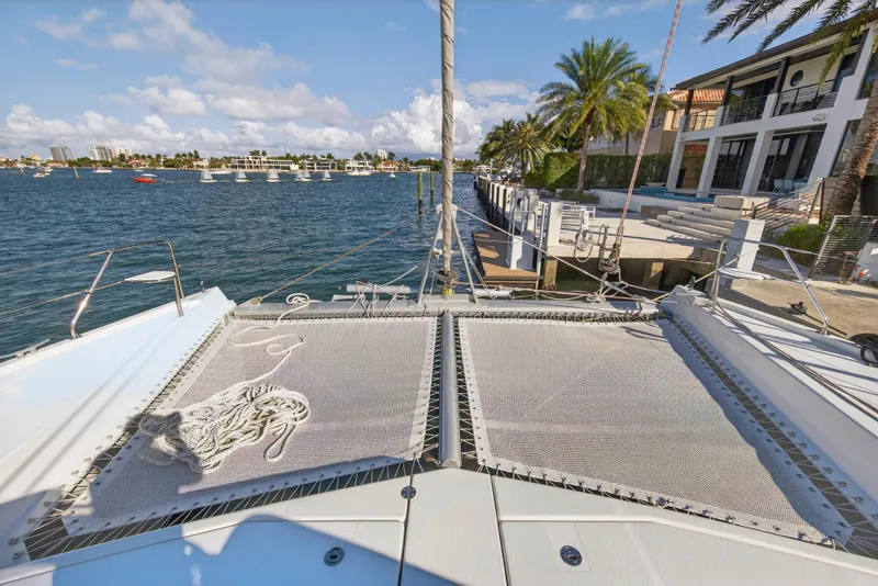 Slide: The Image of 2019 Leopard 58 catamaran docked by waterfront homes, featuring spacious deck and netting. - 23