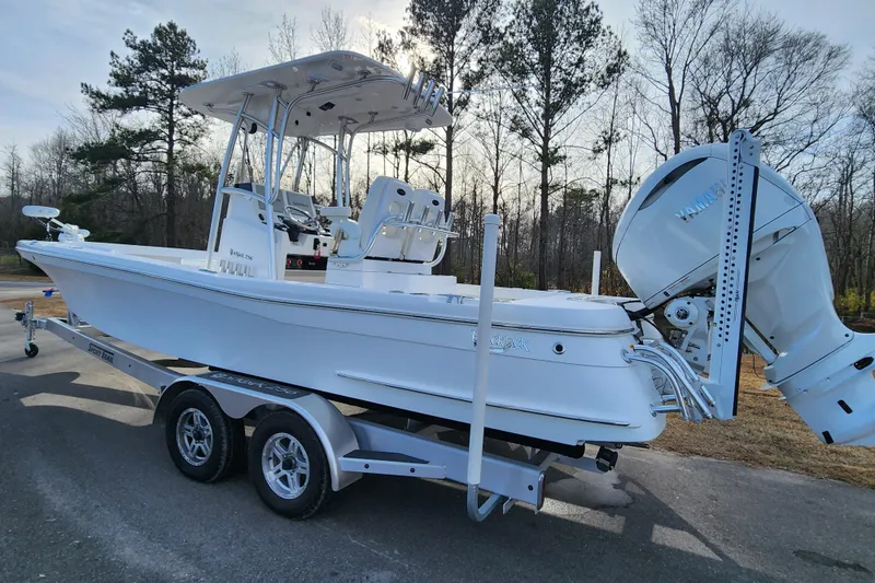 Slide: The Image of 2025 BlackJack 256 Coastal boat on trailer, parked outdoors with trees in background. - 2
