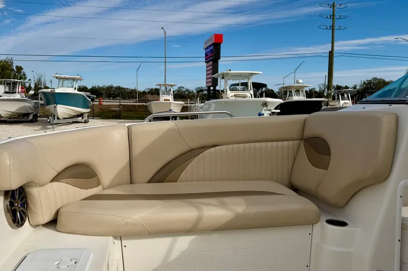 Slide: The Image of 2014 NauticStar 223DC Sport Deck boat interior with beige seating, parked at a marina. - 11