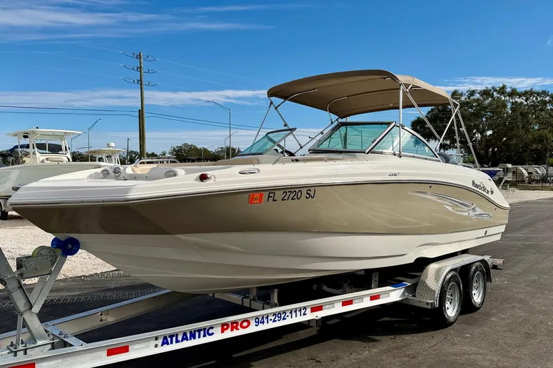 Slide: The Image of 2014 NauticStar 223DC Sport Deck boat on trailer, beige and white, parked outdoors. - 2