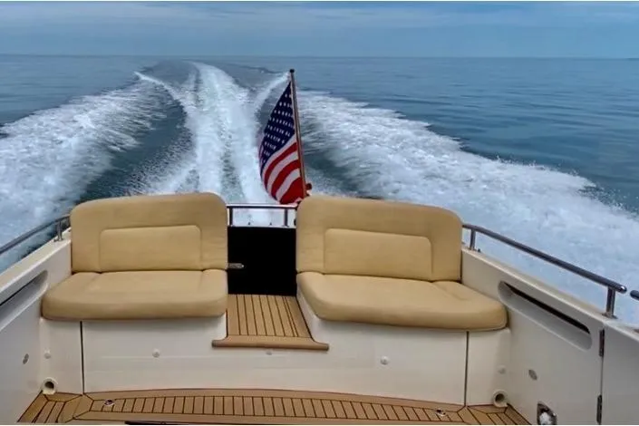 Slide: The Image of 2015 MJM 36z Express boat cruising with American flag, teak deck, and cushioned seating. - 51