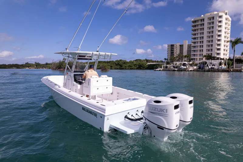 Slide: The Image of 2024 Bluewater 2550 boat with dual Suzuki engines cruising near waterfront buildings. - 14